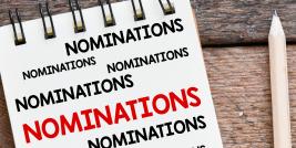 The word 'nominations' on a notepad next to a pencil on a wooden desk