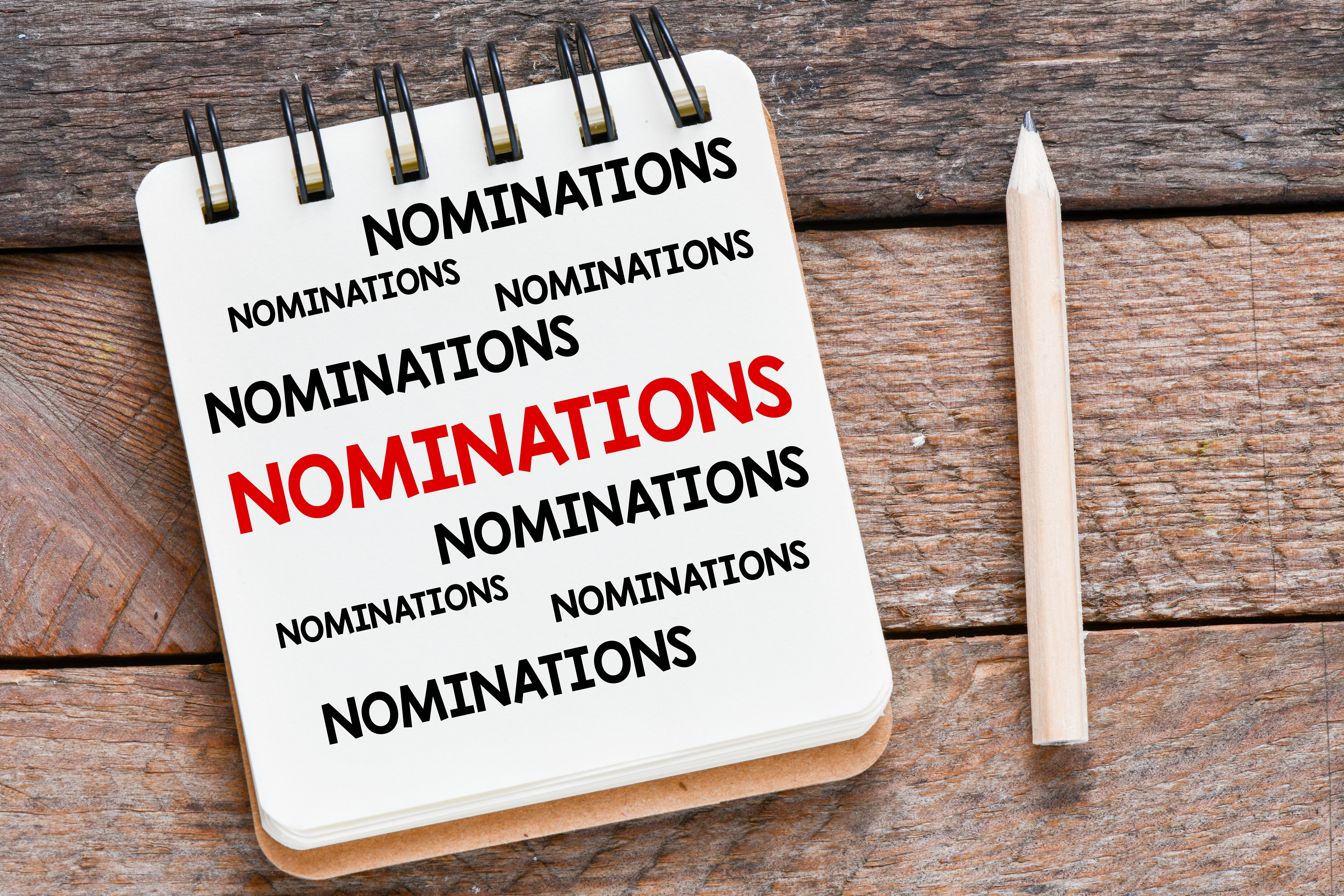 The word 'nominations' on a notepad next to a pencil on a wooden desk